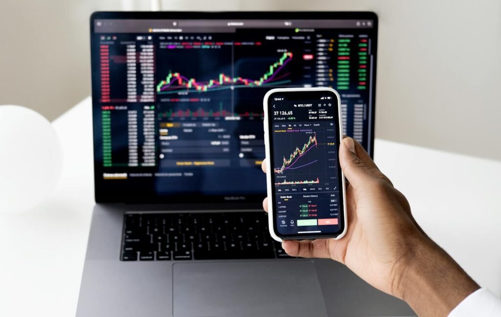 Person checking stock market graphs on laptop and smartphone, focusing on financial data. how to buy your first stock