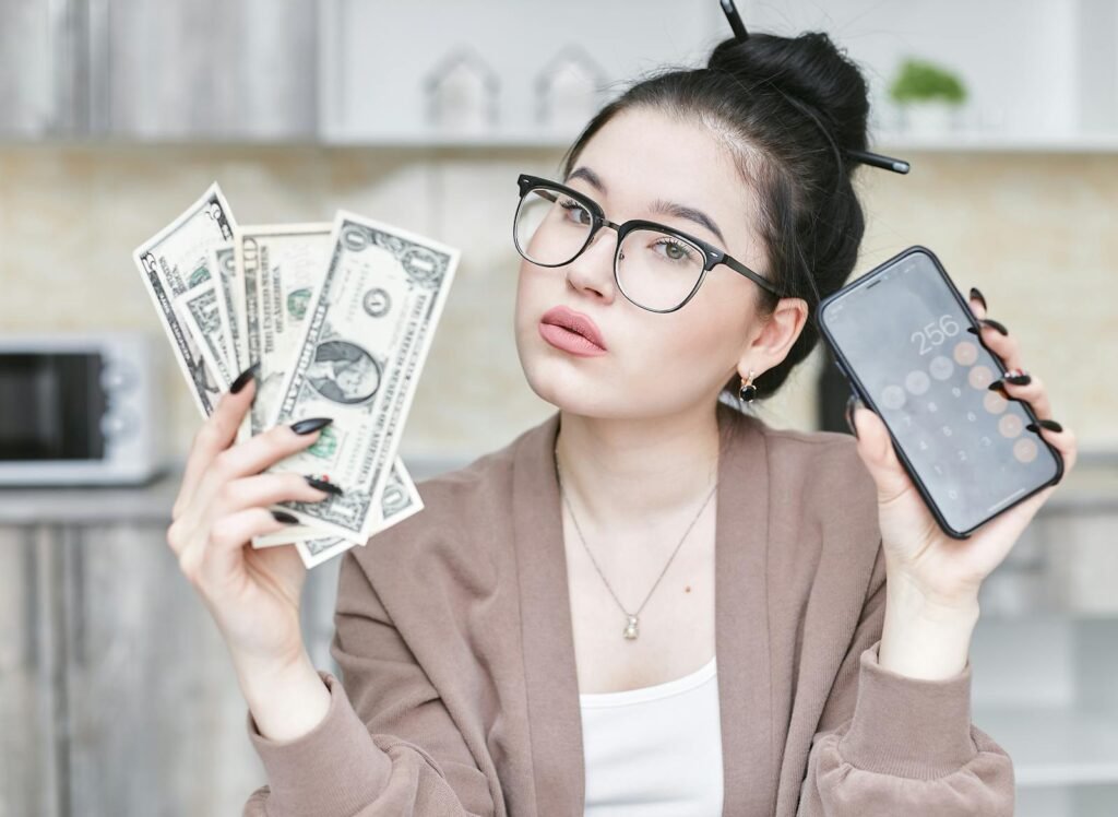 Woman holding cash and smartphone displaying calculator, highlighting personal finance management. most investing advice online is useless